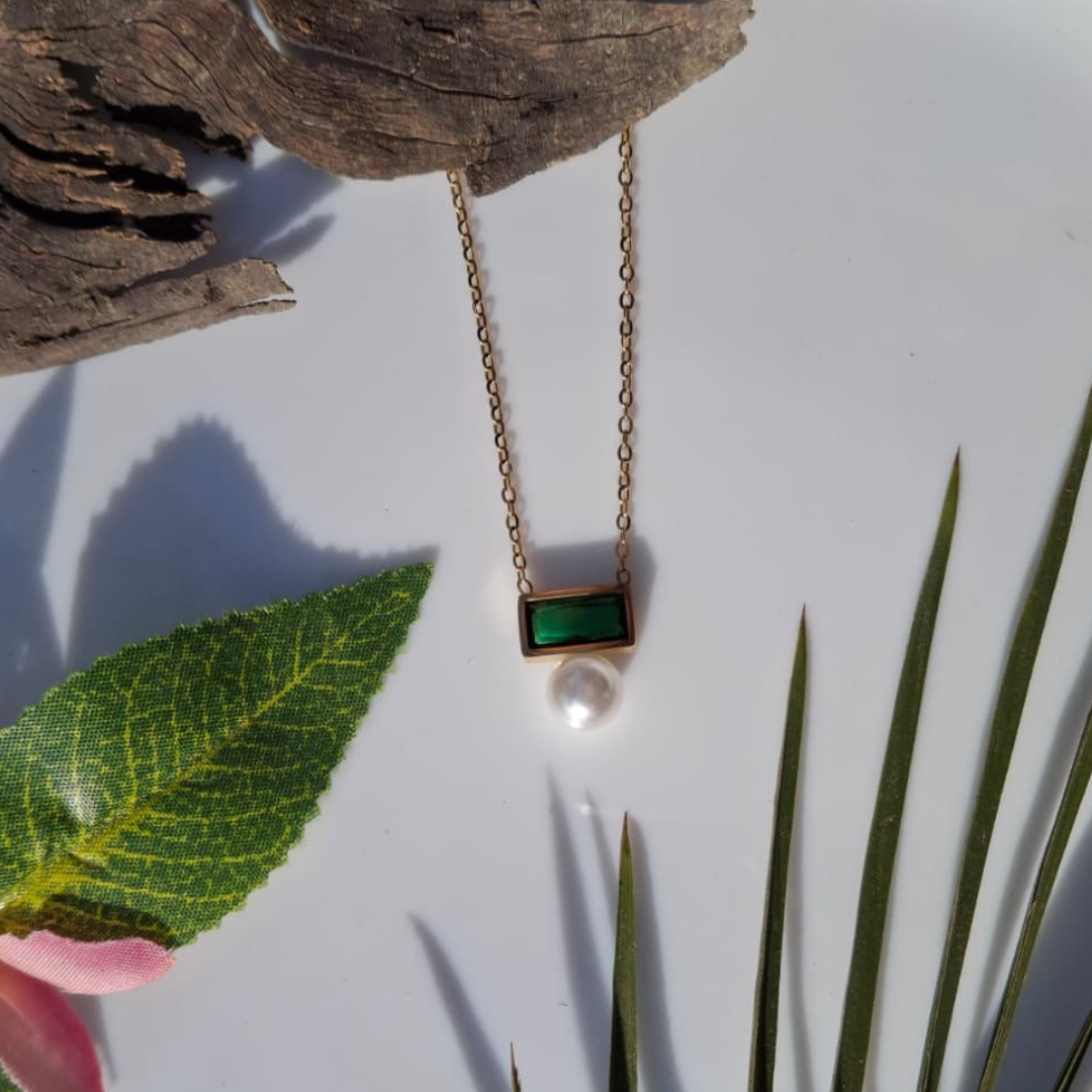 Necklace with a green pendant and pearl on a white surface with leaves and wood.