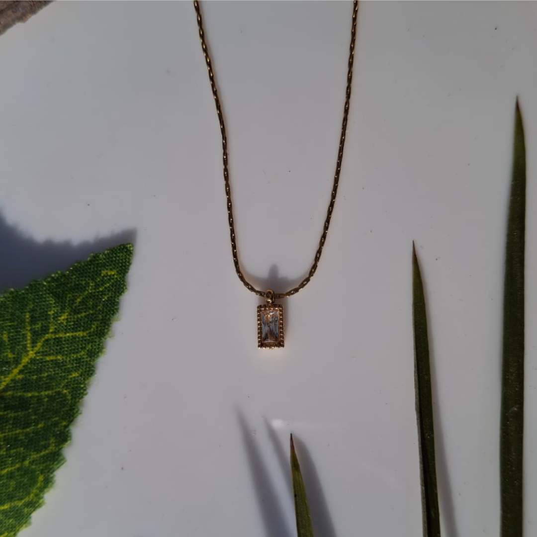 Necklace with a rectangular pendant on a white background with green leaves.