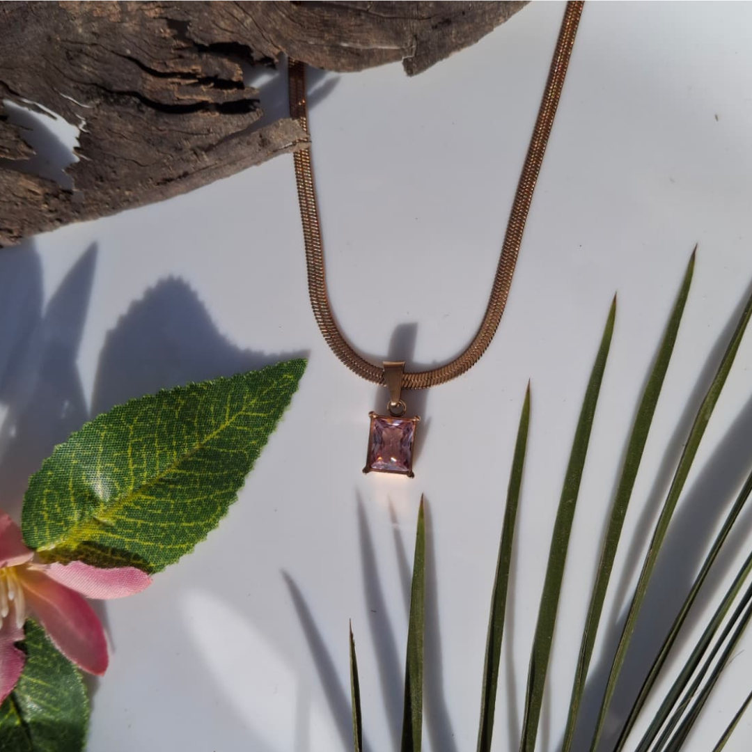 Necklace with a pink gemstone pendant on a white surface with green leaves and a pink flower.